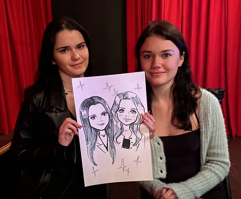 Two guests holding their hand-drawn anime-style portraits on paper